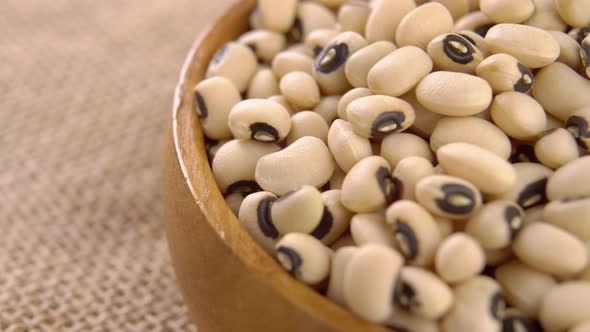 Kidney black eyed beans in rustic wooden bowl on burlap. Dry uncooked legumes. Macro