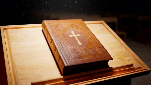 Holy Bible on a wooden table lightened by rays of light falling in the chapel.