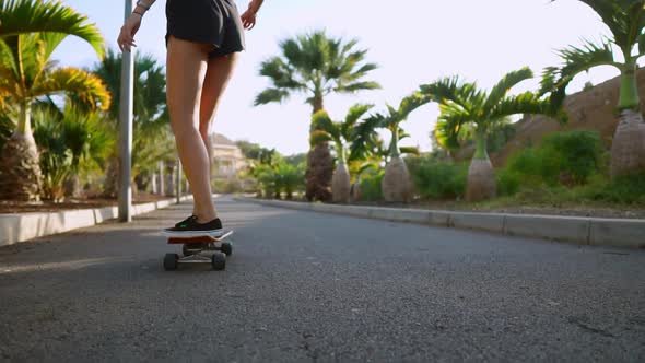 Girl in Slow Motion Rides a Skateboard in the Park with Palm Trees