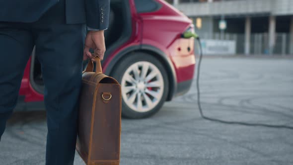 Man with Suitcase Standing Near Electric Car That Charging