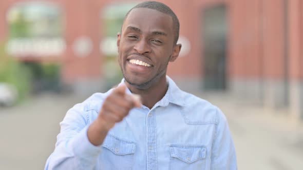 Outdoor Portrait of Cheerful African Man Pointing at the Camera