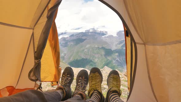 Persons Lie in Tent and Wave Legs in Boots Against Mountains