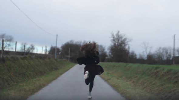 Young woman running away outside on the isolated road during misty weather.