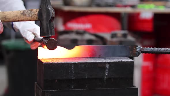 Blacksmiths forging hot metal with hammer in workshop
