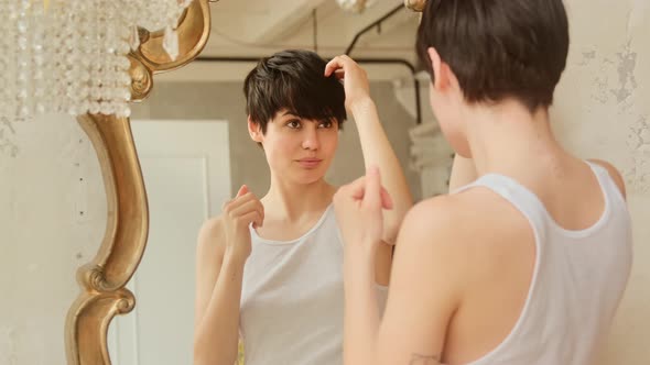 Woman looks in the mirror, wears a care oil on the ends of her hair and straightens her hairstyle