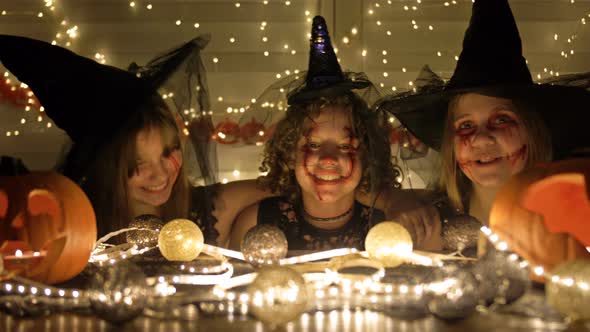 Three Teenage Girls in Black Witch Costumes with Frightening Makeup on Their Faces Are Sitting at a