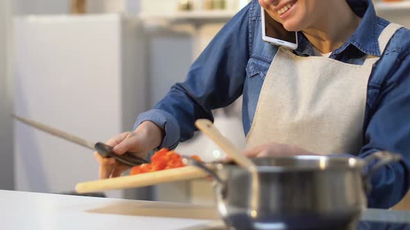 Housewife Cutting Tomato and Adding Into Saucepan While Talking on Mobilephone