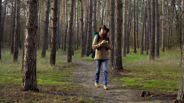 A Man in a Hat with a Backpack Takes Pictures in the Forest