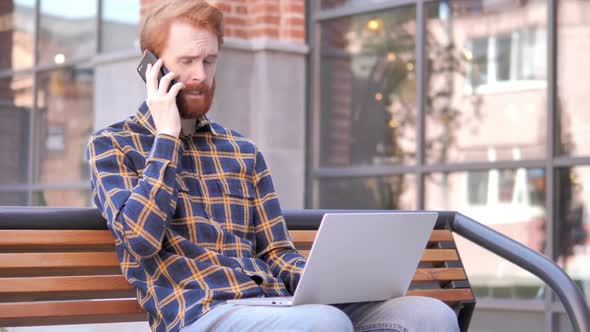 Redhead Beard Young Man Talking on Phone Sitting on Bench