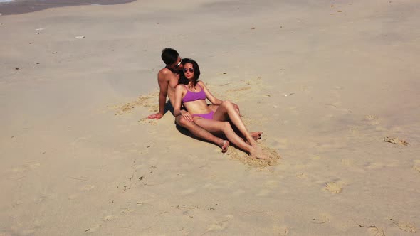 Isolated young couple in love smiling in front of sunny rays, sunbathing on sand of exotic beach