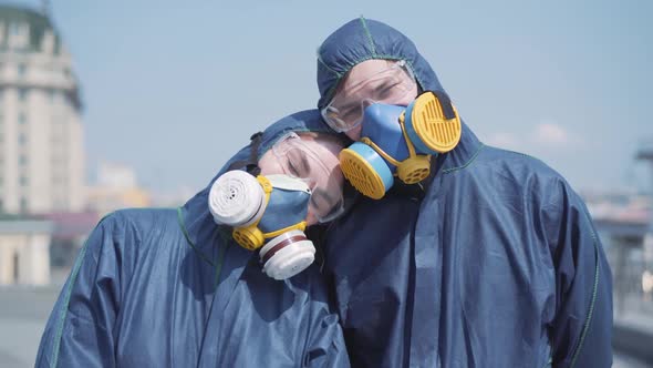 Camera Approaching To Smiling Young Couple in Respirators and Protective Eyeglasses Posing Outdoors