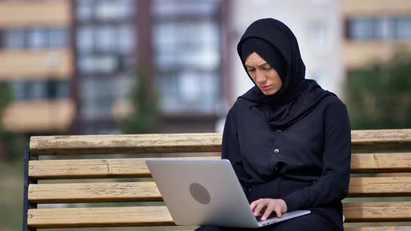 Focused Freelancer Modern Muslim Woman Working Use Laptop Outdoor Sitting on Bench at City Building