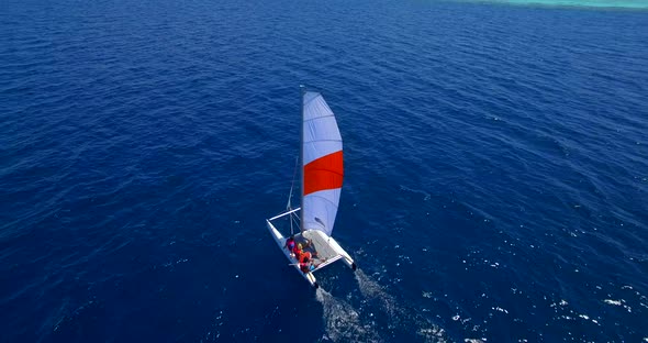 Aerial drone view of a man and woman sailing on a boat to a tropical island.