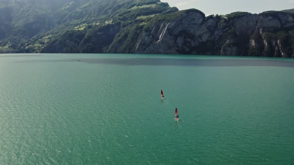 Two Men are Windsurfing on a Lake at the Foot of the Alps in Switzerland