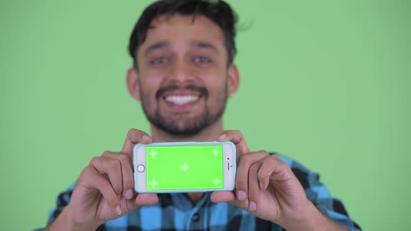 Face of Happy Young Bearded Persian Hipster Man Showing Phone