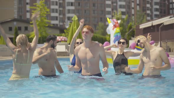 Happy Smiling Tourists Dancing and Splashing Water in Pool on Sunny Day. Portrait of Young Cheerful