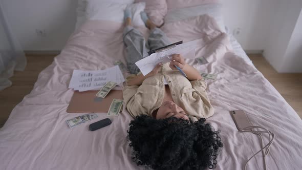 High Angle View of Concentrated Woman Writing on Business Graph Lying on Cozy Bed Indoors