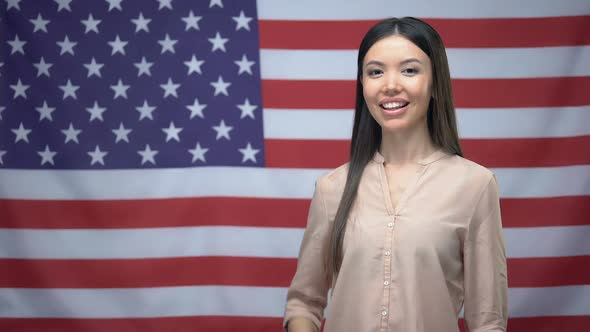 Happy Asian Woman Showing Thumbs-Up and Winking Against USA Flag Background