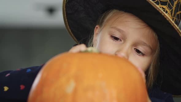 Little girl in witch costume drawing on pumpkin