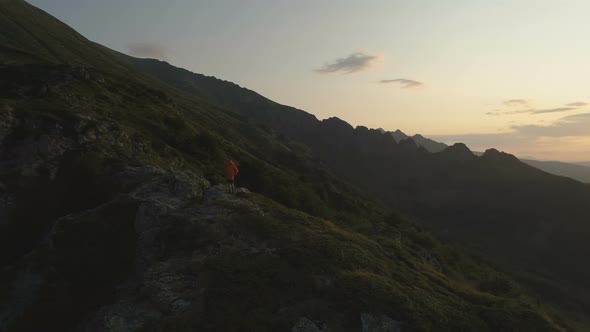 Man Standing Over the Precipice in the Mountains Looking the Sunset