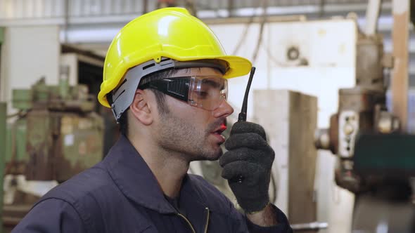 Factory Worker Talking on Portable Radio While Inspecting Machinery Parts