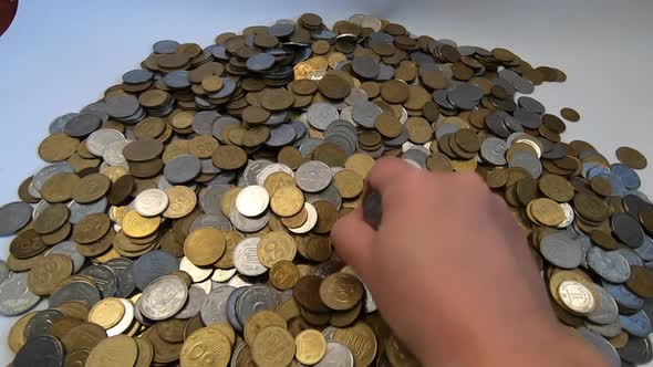 Girl Picks Up Handful of Coins in Her Hand and Throws It Over Coins on Table