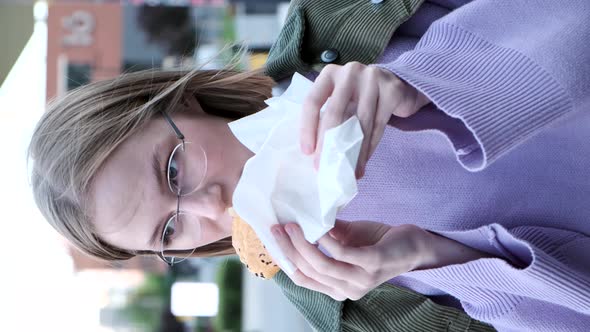 Delighted Young Woman with Short Hair Eats Burger in Cafe