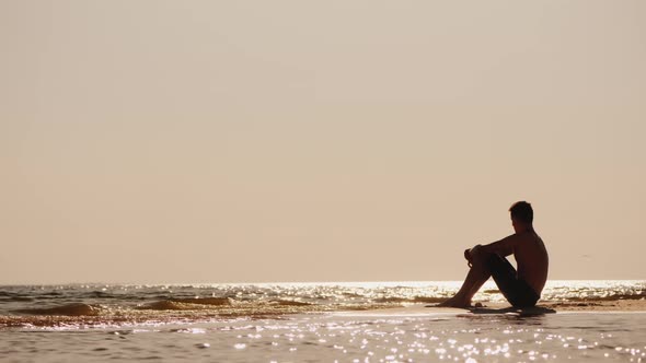 Lonely Silhouette of a Young Man Sitting on the Sand By the Sea