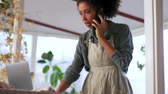 Serious African woman talking by phone and looking at laptop