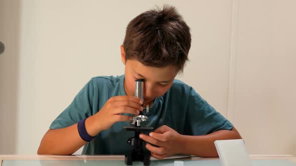 Curious Darkhaired Teenage Boy is Looking Through a Microscope