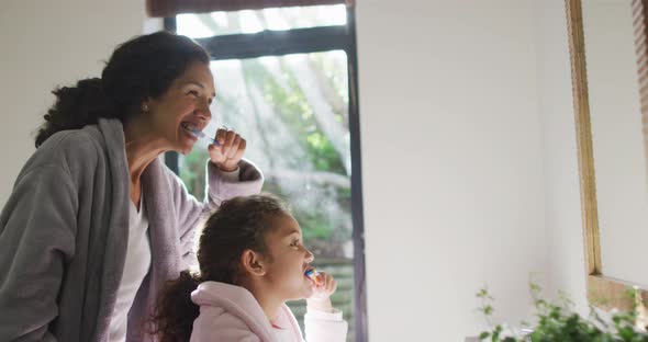 Happy mixed race mother and daughter brushing teeth in bathroom