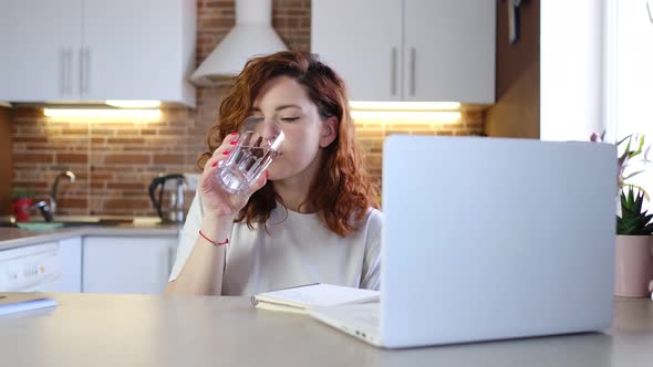 Young Woman Drinking Water While Working with Her Laptop in Home Office