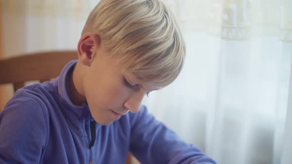 A schoolboy draws a window. A close-up of the boy draws at the table