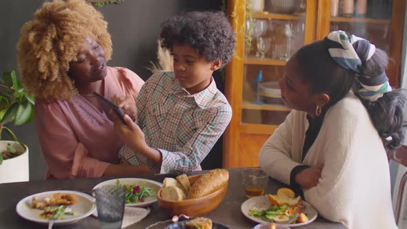 Kid Showing Picture on Tablet to Family at Home Dinner