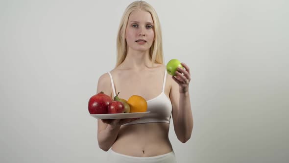 A Woman Holds a Plate of Fruit Takes a Green Apple and Eats