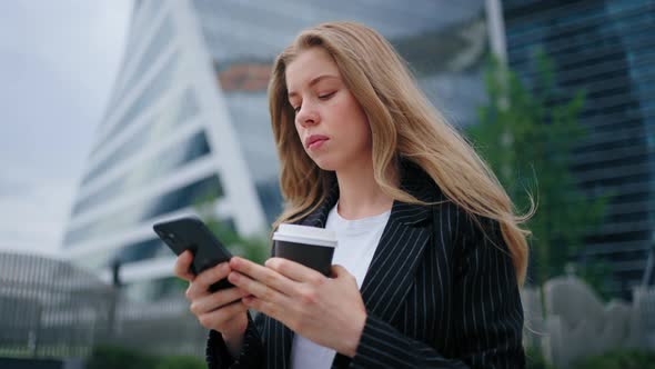 Successful Young Beautiful Woman with Phone and Coffee Cup Walking Between Business Buildings with