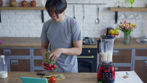 Cheerful Asian Man with Toothy Smile Cooking Healthful Salad and Talking at Tablet Web Camera