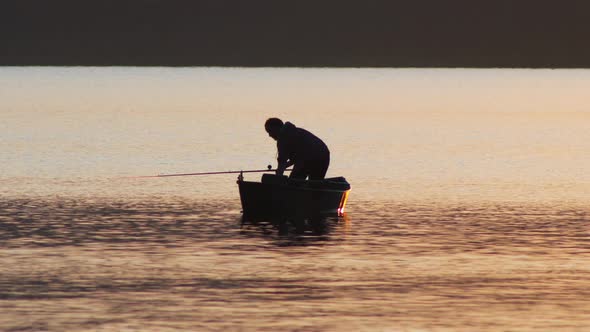 A Silhouette of Man Sitting in a Boat and Fishing on Sunset