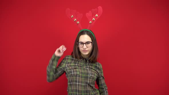 A Young Woman Is Dancing with a Headband in the Form of Christmas Antlers. Studio Shooting on a Red