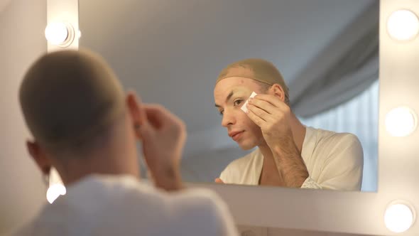 Concentrated Queer Woman in Wig Cap Applying Eye Paper Patch on Face in Slow Motion Reflecting in