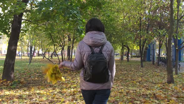 A Brunette Woman in a Brown Jacket and a Bouquet of Leaves Is Walking in the Park, The Camera