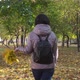 A Brunette Woman in a Brown Jacket and a Bouquet of Leaves Is Walking in the Park, The Camera - VideoHive Item for Sale