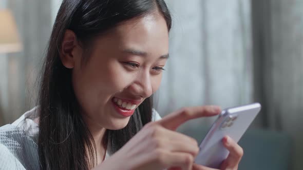 Close Up Of Smiling Asian Female Footwear Designer Using Smartphone While Working On A Laptop