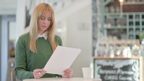 Attractive Young Woman Celebrating Success While Reading Documents in Cafe
