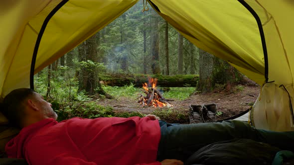 A Tourist Lies in a Tent and Looks at a Fire in the Forest