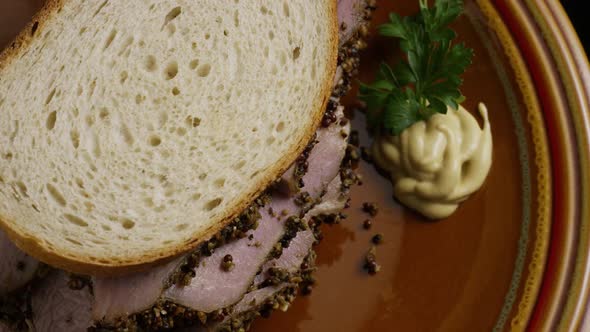 Rotating shot of delicious, premium pastrami sandwich next to a dollop of dijon mustard 