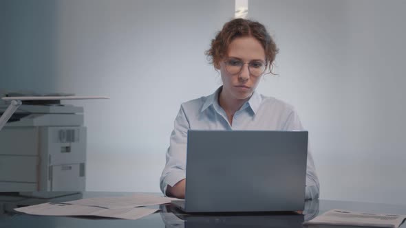 Concentrated Businesswoman Sitting on Workplace in Office Typing on Laptop