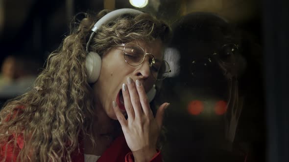 A Curly Woman in Headphones is Falls Asleeping and Yawning After Hard Work Day in Bus