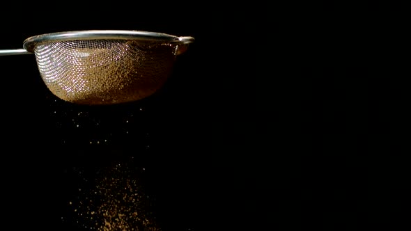 Light Brown Powder Sifting with Sieve, Slow Motion Isolated on Black Background