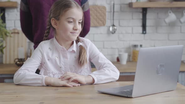 Portrait of Cute Caucasian Female Teenager Looking at Laptop Screen, Holding Head with Hand and